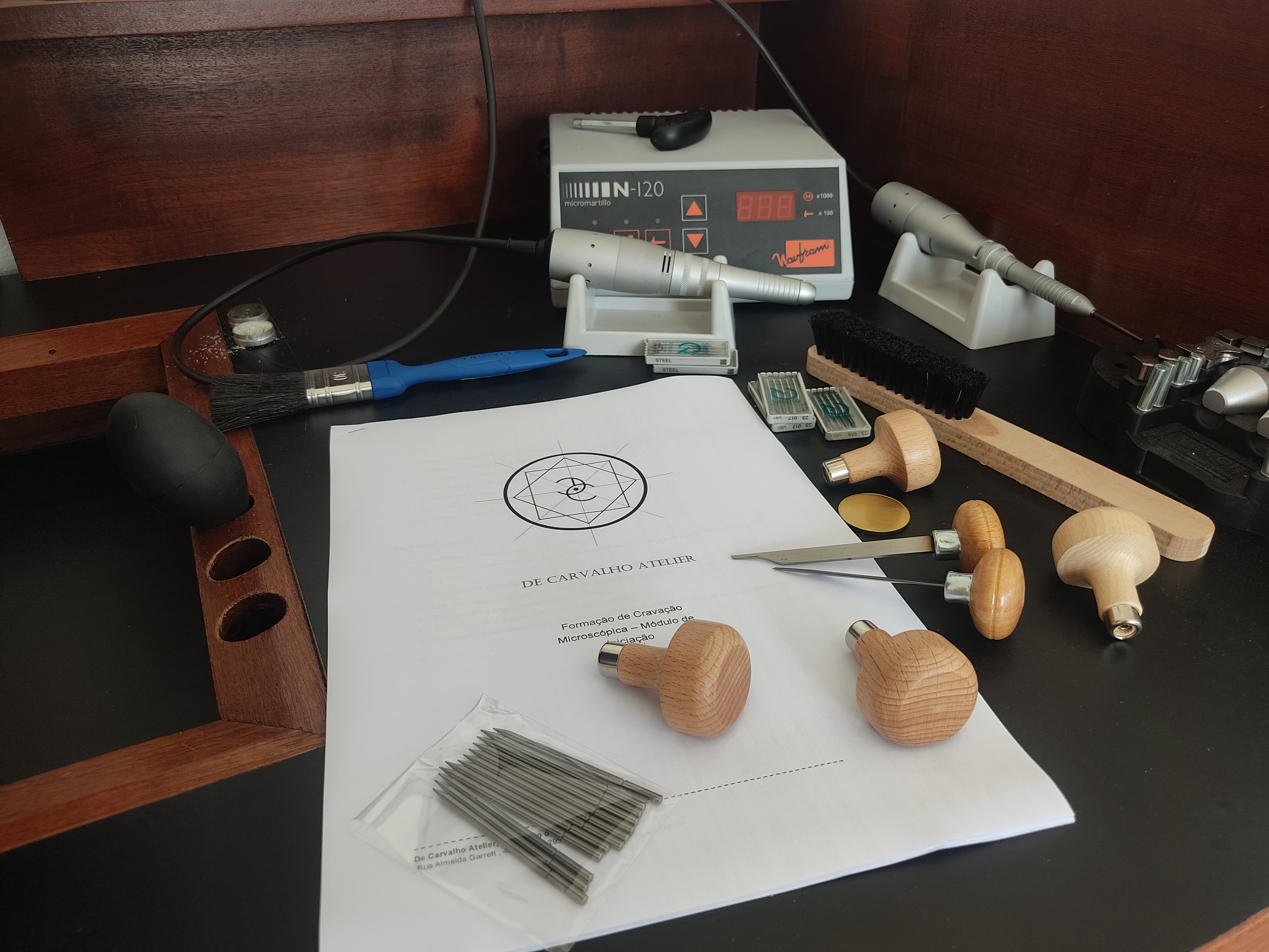 Ferramentas e caderno De Carvalho na bancada — módulo de iniciação em cravação microscópica